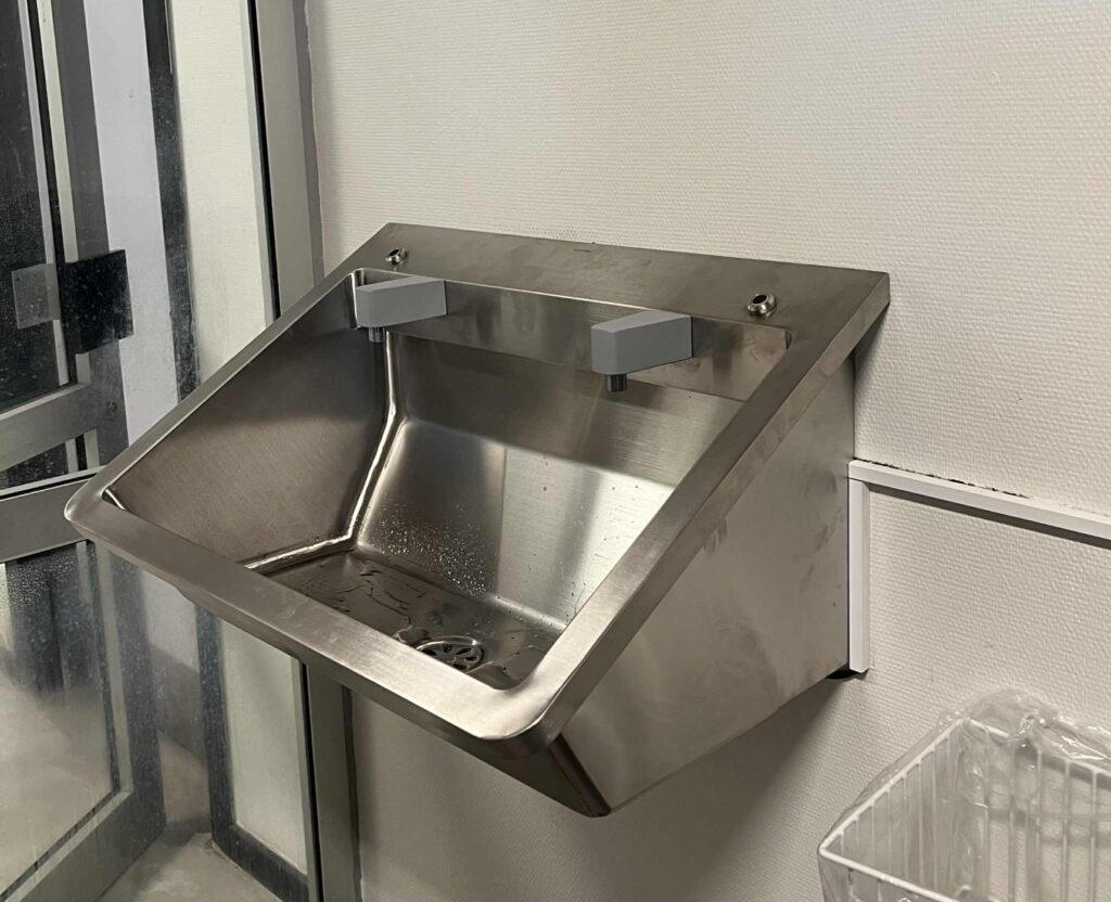 Rustfrit stålvask på væg i sanitetsrum